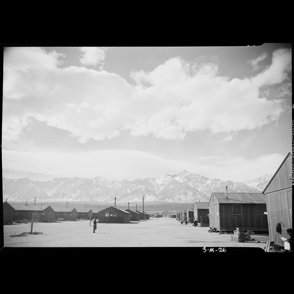 Manzanar street, with temporary housing structures, in a Japanese relocation center in California, mountains are visible in the background.