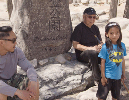 Three Generation of director Tadashi Nakamura's family seated around a stone monument in a Japanese garden.